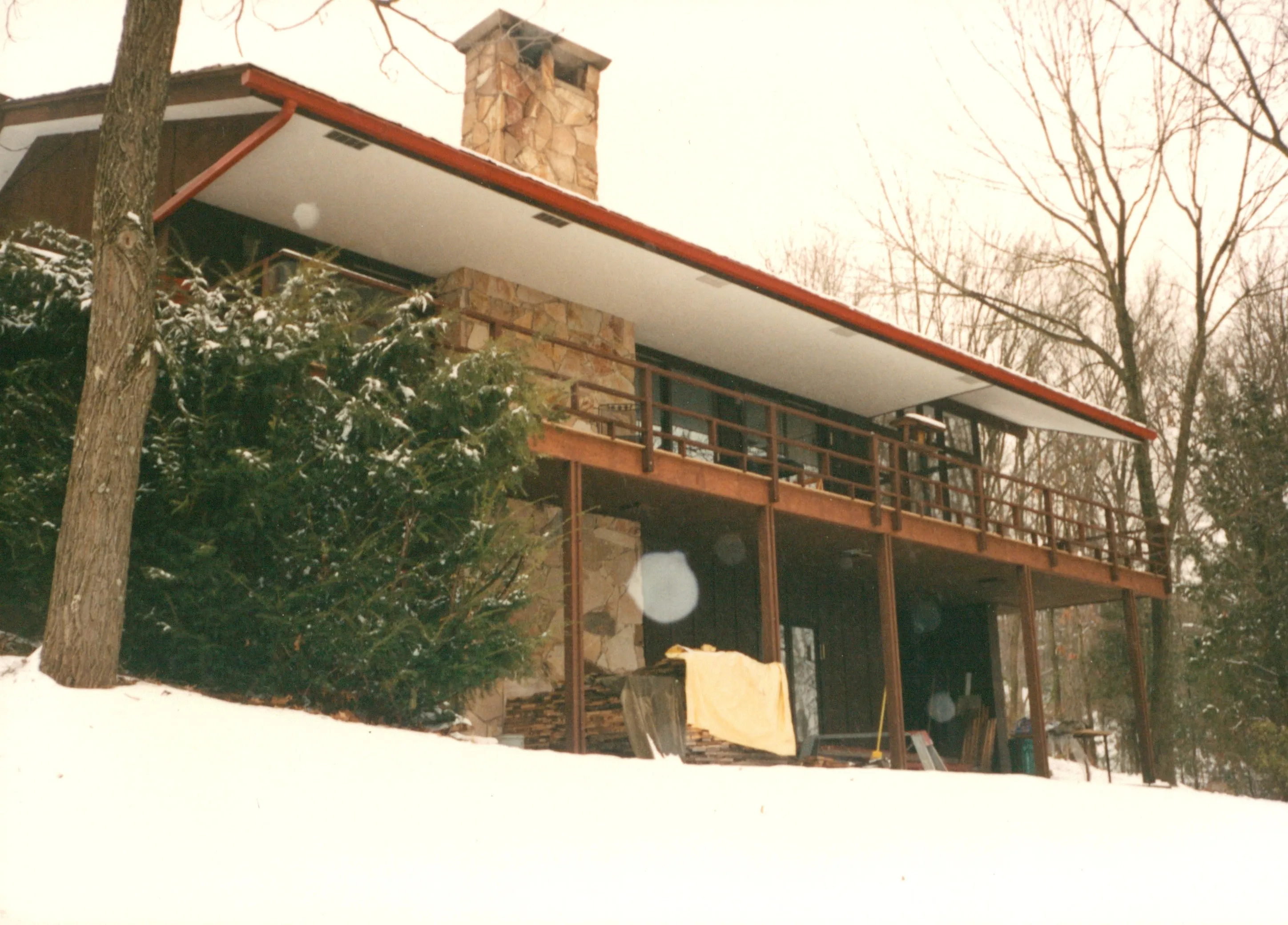 House exterior showing deep overhanging eave trimmed in red, fieldstone chimney, and raised deck