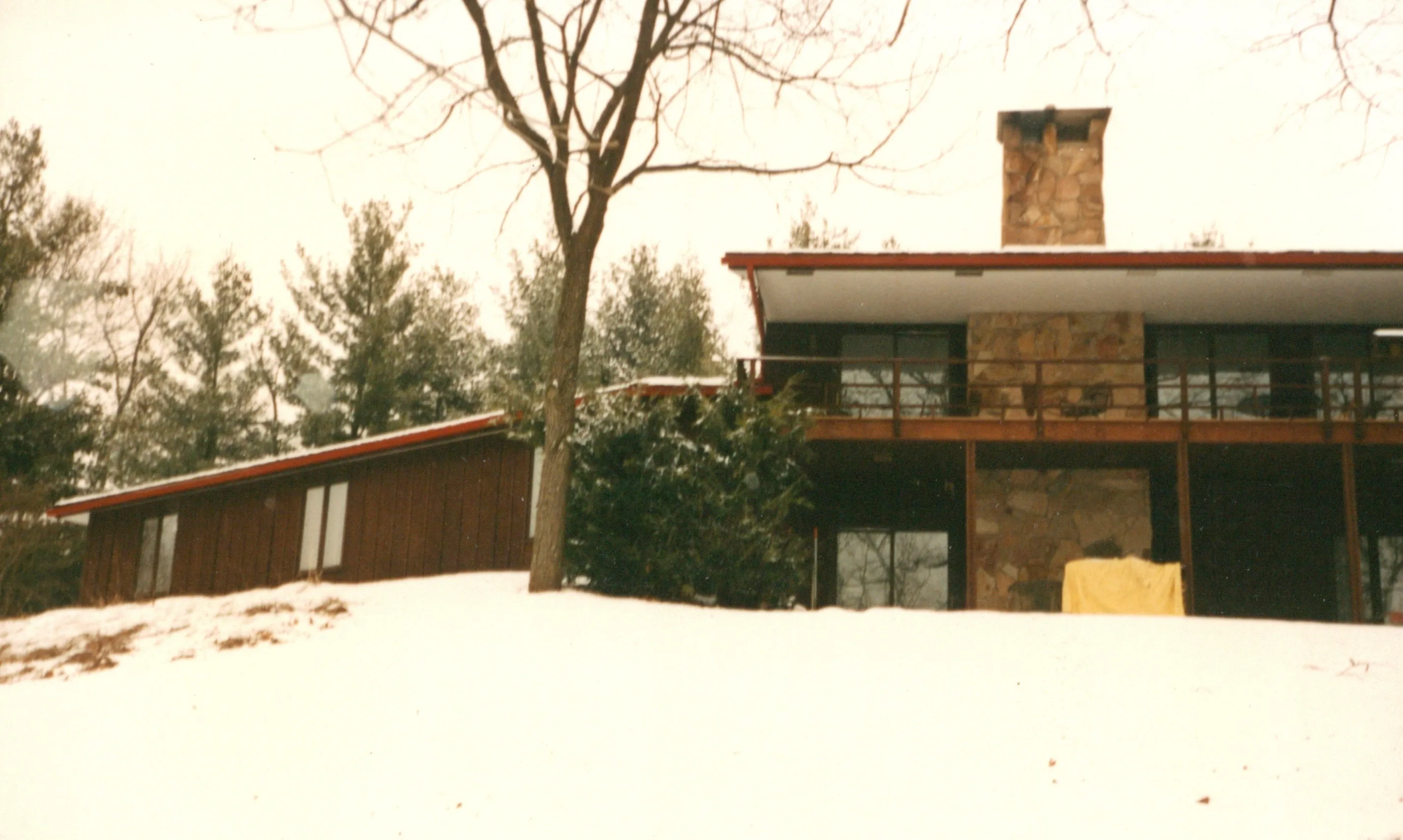 Second exterior view of the low wide roofline, stone chimney, and post-and-beam deck