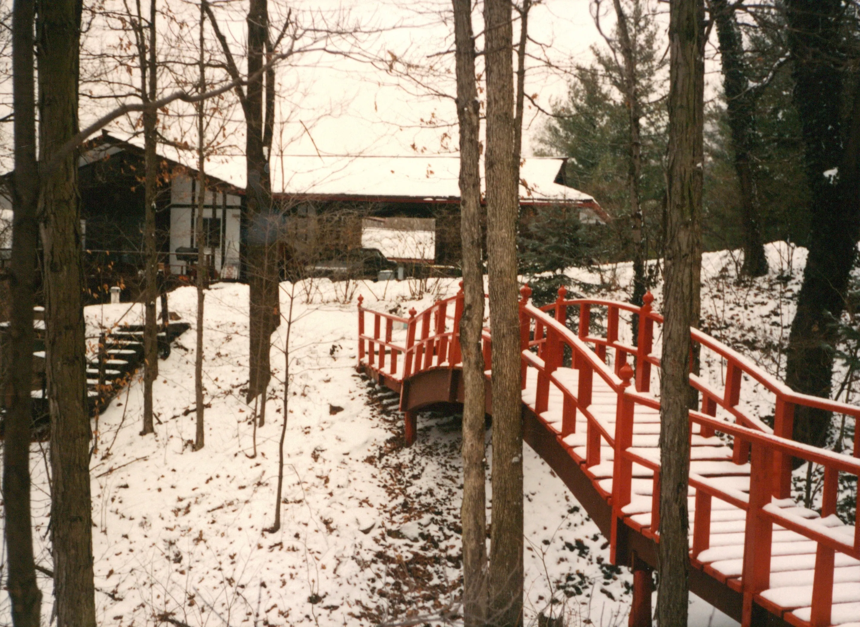 Second view of the red bridge angling toward the house through bare trees