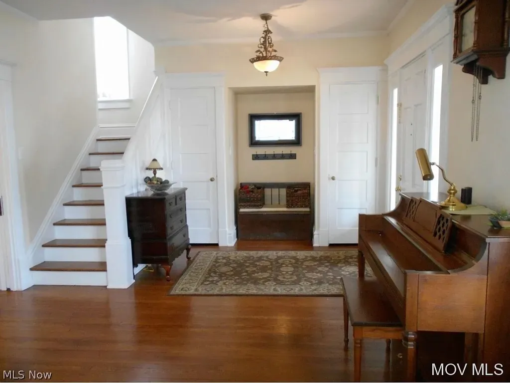 <strong>651 Sixth Street, Marietta — exterior and interior in a c. 2015–2020s real-estate listing.</strong> Three frames from a Mid-Ohio Valley MLS listing retrieved by Chuck Eesley 2026: the front of the house with '651' visible on the porch column; the side view showing the side entrance and garage; and the entryway with the staircase, hardwood floors, antique chest, grandfather clock, and piano. The architecture and renovation visible are consistent with the house Charlie's autobiography describes — an older two-story with a substantial front porch, the kind Will the architect would have bought to redesign around the family. The 1965 autobiography's 'playroom' completion would have been on the second floor; the staircase visible in the entryway is the same one his sisters Jeanne and Anne climbed from their old-upstairs-kitchen bedroom.