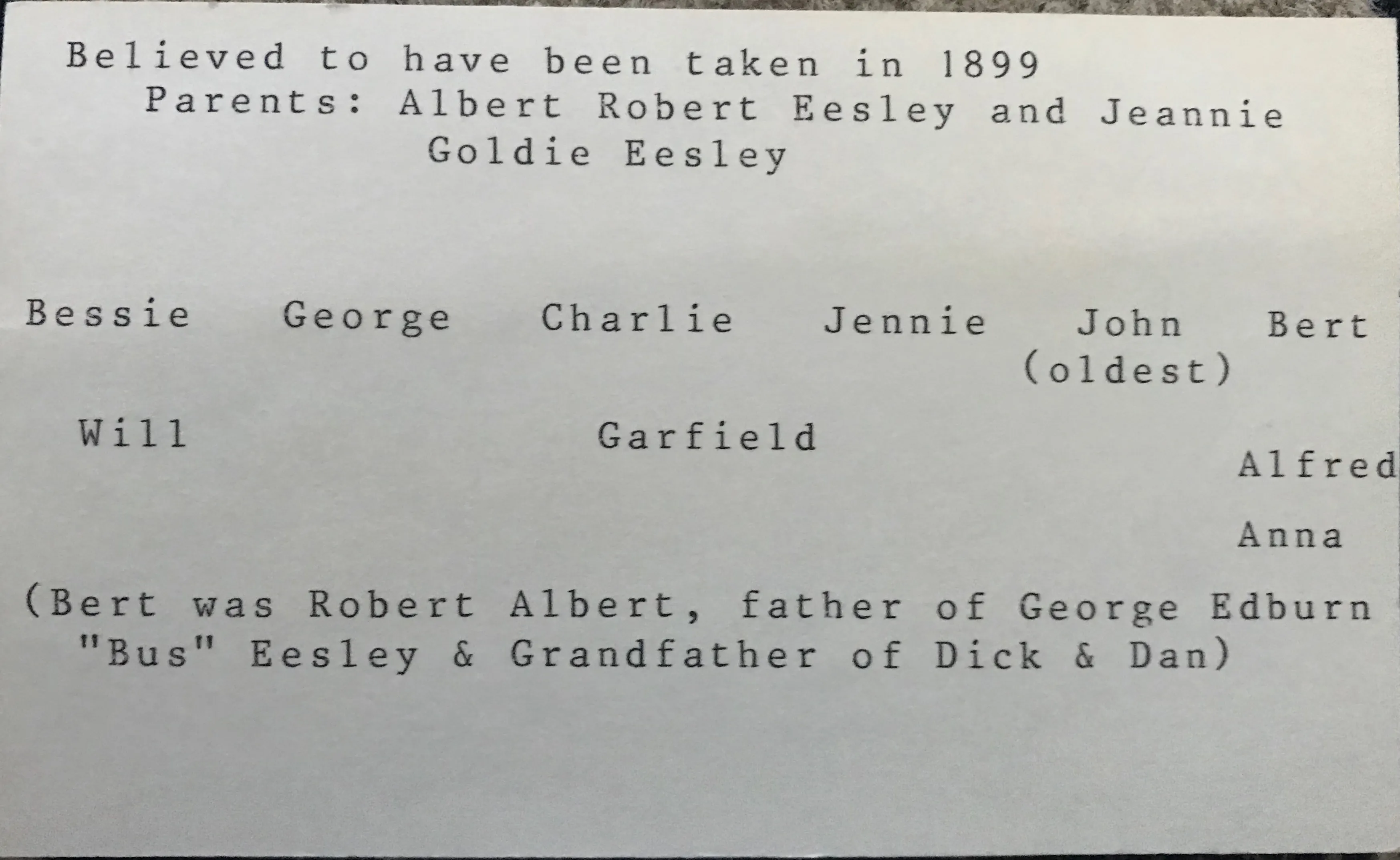 A typed caption key for the 1899 portrait, listing the parents and all ten children by first name — Bessie, George, Charlie, Jennie, John (oldest), Bert, Will, Garfield, Alfred, Anna — with the note that "Bert was Robert Albert, father of George Edburn 'Bus' Eesley & Grandfather of Dick & Dan."