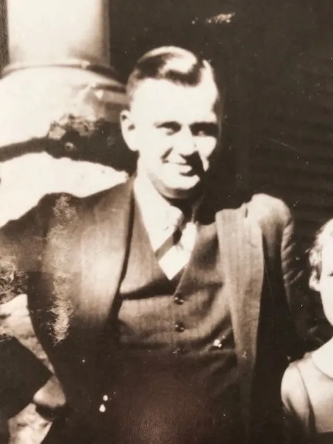 George Edburn "Bus" Eesley, a man of about forty in a three-piece suit, smiling; one of his young children stands at the edge of the frame.