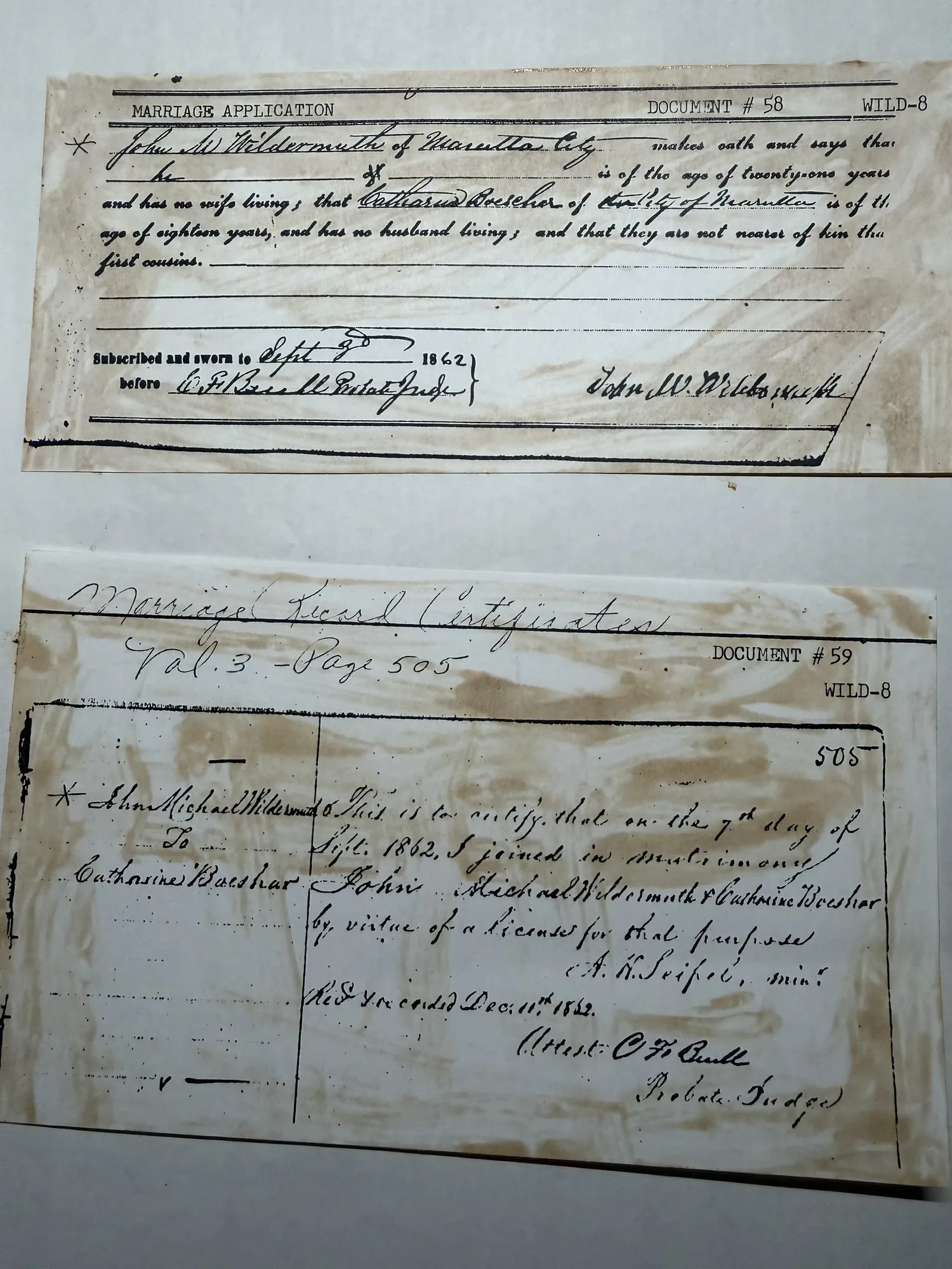 A photograph of two Washington County marriage documents laid one above the other, browned and stained, the upper a printed marriage application form marked DOCUMENT #58 WILD-8 completed in ink for John M. Wildermuth of Marietta City and Catharina Boeshar, sworn before C. F. Buell, Probate Judge, and signed by the groom; the lower a handwritten marriage record certificate marked DOCUMENT #59 WILD-8, headed Marriage Record Certificates Volume 3 page 505, certifying the matrimony of John Michael Wildermuth and Catharine Boeshar on the 7th day of September 1862 by a minister, received and recorded in December 1862, attested by the Probate Judge.