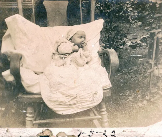 Ruth Irene Wildermuth as an infant, bundled in a rocking chair in a leafy yard; the print is dated 5 July 1922.