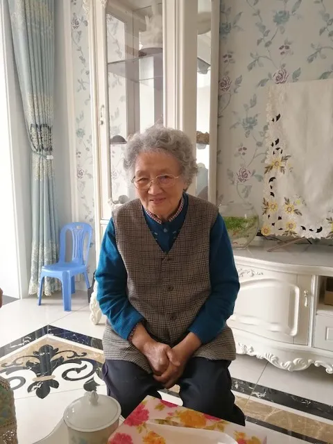 Shang Yaozhen at home in Qingdao, seated in a floral-papered sitting room.