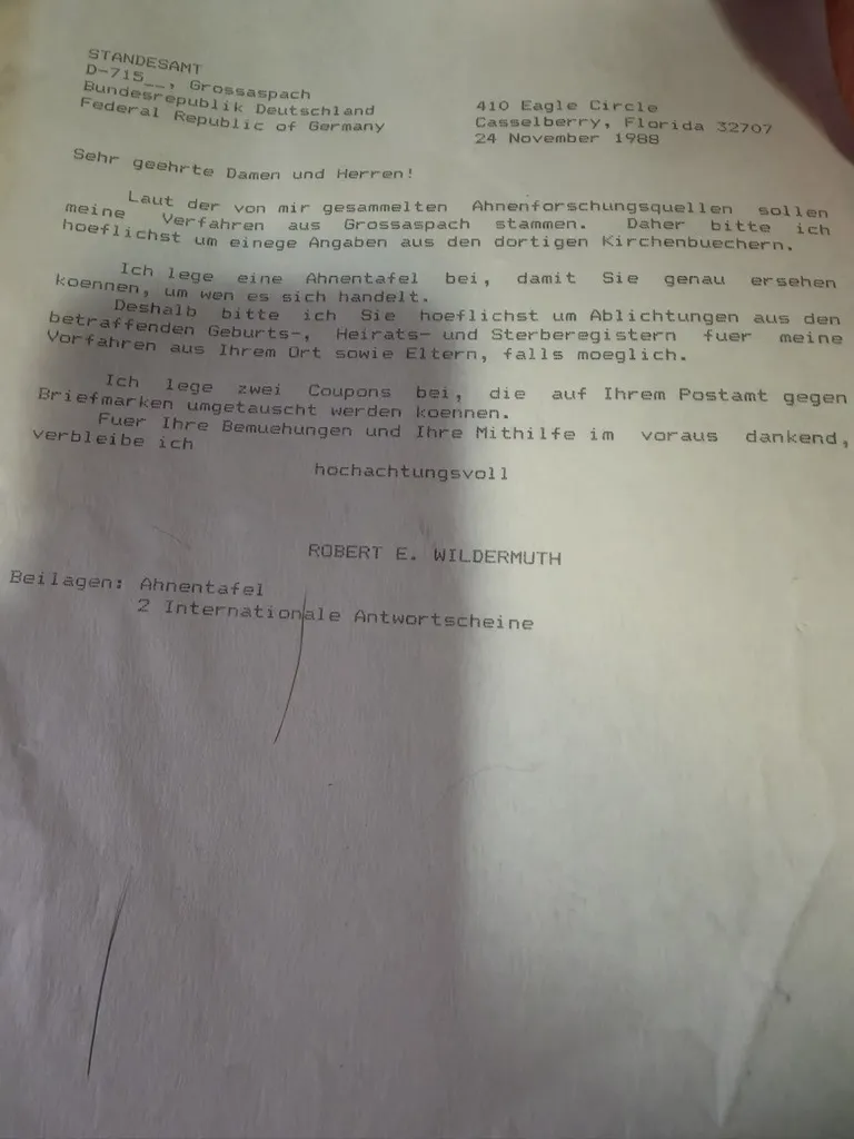 A typed letter in German dated 24 November 1988 from Robert E. Wildermuth of Casselberry, Florida to the Standesamt at Grossaspach, stating that his ancestors are said to come from Grossaspach, enclosing an Ahnentafel so the office can see exactly who is meant, requesting photocopies from the relevant birth, marriage and death registers, and enclosing two international reply coupons.
